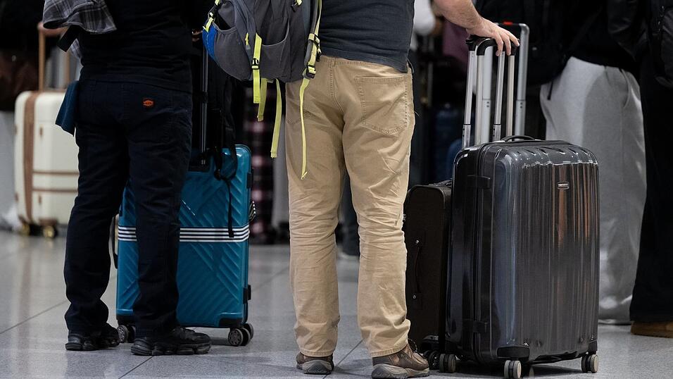 Passagiere stehen am M&uuml;nchner Flughafen mit ihrem Gep&auml;ck an einem Check-in-Schalter.