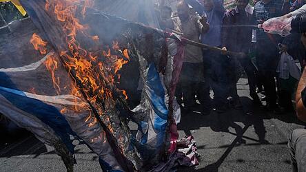 Iranische Demonstranten verbrennen eine israelische und eine US-amerikanische Flagge während einer Demonstration zur Verurteilung israelischer Angriffe auf mehrere Städte im Iran.