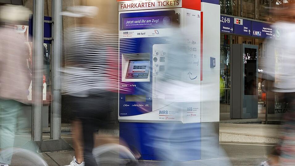 Passagiere gehen an einem Bahnhof an Fahrkartenautomaten vorbei.