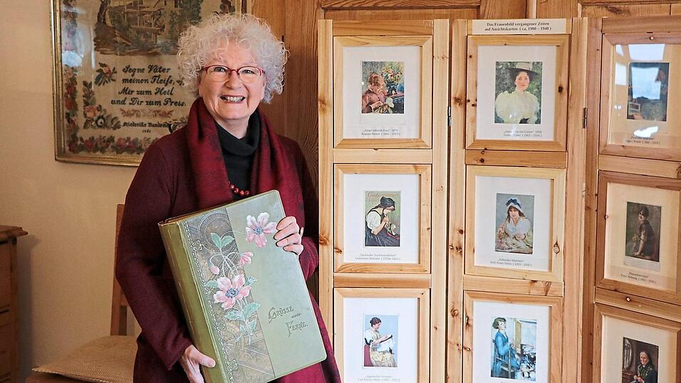 Gudrun Linn mit einem alten Album voller Postkarten, eines ihrer Lieblingsst&uuml;cke der neuen Ausstellung, daneben Frauenportr&auml;ts auf Postkarten aus dem 19./20. Jahrhundert.