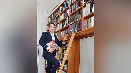 Felix Weiland inmitten der Verlagsbibliothek in der Leibnitzstra&szlig;e. In der Hand h&auml;lt er den ersten Ausstellungskatalog, f&uuml;r den er alleine verantwortlich war, der vor Kurzem ver&ouml;ffentlicht wurde, zur Landesausstellung in Baden-W&uuml;rttemberg.