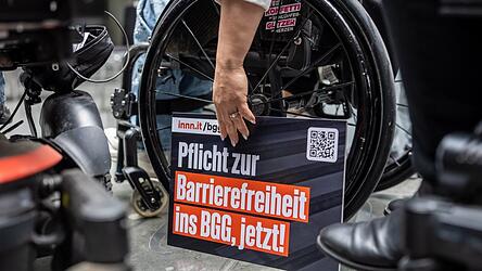Ein Schild mit der Forderung &bdquo;Pflicht zur Barrierefreiheit ins BBG, jetzt!&ldquo; steht bei der &Uuml;bergabe einer Petition zur Reform des Behindertengleichstellungsgesetzes am Rad eines Rollstuhls.