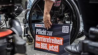 Ein Schild mit der Forderung „Pflicht zur Barrierefreiheit ins BBG, jetzt!“ steht bei der Übergabe einer Petition zur Reform des Behindertengleichstellungsgesetzes am Rad eines Rollstuhls. Ein Schild mit der Forderung „Pflicht zur Barrierefreiheit ins BBG, jetzt!“ steht bei der Übergabe einer Petition zur Reform des Behindertengleichstellungsgesetzes am Rad eines Rollstuhls.