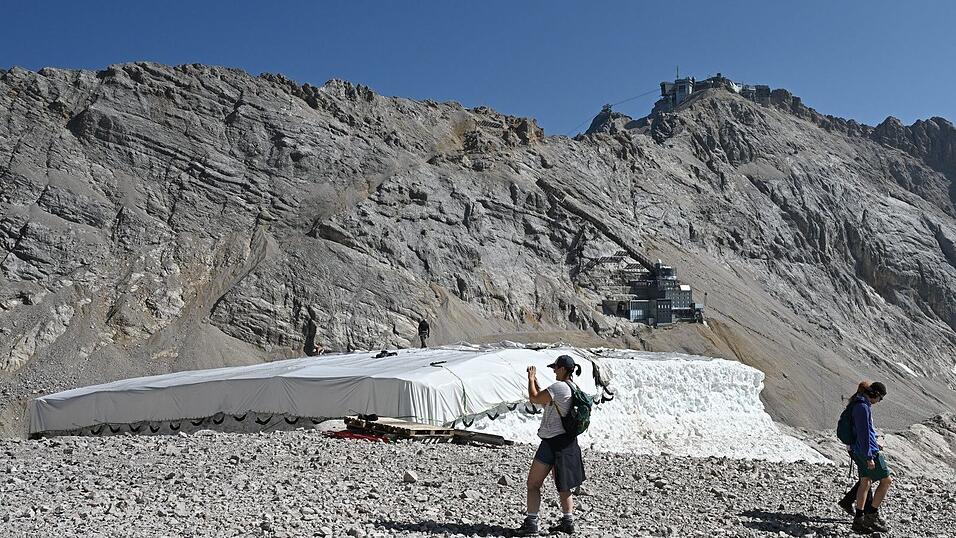 Eine Person macht Fotos neben Abdeckfolien auf einem Schneedepot neben den &Uuml;berresten des N&ouml;rdlichen Schneeferner-Gletschers auf der Zugspitze.