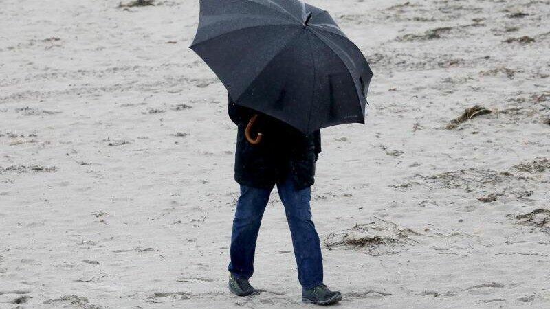 Spaziergänger mit wetterfester Kleidung und Regenschirm am Ostseestrand.