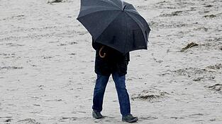 Spaziergänger mit wetterfester Kleidung und Regenschirm am Ostseestrand.