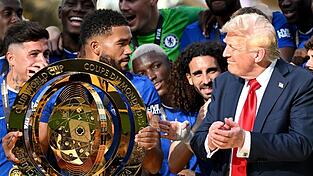 Chelseas Kapitän Reece James (l/vorn) hält auf dem Siegerpodest die Trophäe in den Händen und schaut irritiert zu US-Präsident Donald Trump.
