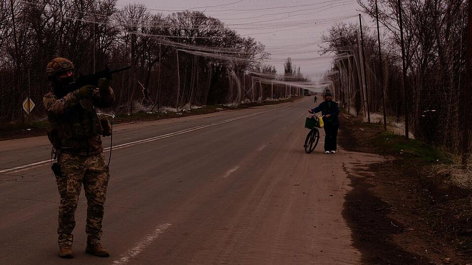 &Uuml;ber der Stra&szlig;e h&auml;ngt ein Netz aus d&uuml;nnen F&auml;den, das Sprengstoff-Drohnen abhalten soll. Ruslan posiert mit seinem Gewehr, eine Frau wei&szlig; nicht so recht, wo sie mit ihrem Rad hinsoll. Nur noch wenige Zivilisten sind in den oft in gro&szlig;en Teilen zerst&ouml;rten D&ouml;rfern geblieben.