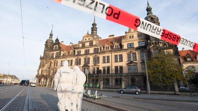 Zwei Mitarbeiter der Spurensicherung stehen vor dem Residenzschloss mit dem Gr&uuml;nen Gew&ouml;lbe hinter einem Absperrband.