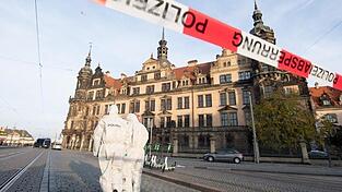Zwei Mitarbeiter der Spurensicherung stehen vor dem Residenzschloss mit dem Gr&uuml;nen Gew&ouml;lbe hinter einem Absperrband.