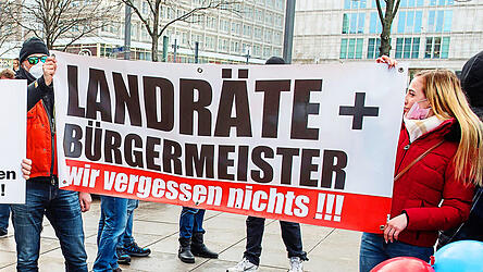 Das Foto zeigt eine Demonstration gegen die Schutzma&szlig;nahmen zur Eind&auml;mmung der Corona-Pandemie auf dem Berliner Alexanderplatz 2022. Ein Transparent mit der Drohung: &bdquo;Landr&auml;te und B&uuml;rgermeister, wir vergessen nichts.&ldquo; Die Corona-Pandemie stellt f&uuml;r viele Kommunalpolitiker einen Wendepunkt dar. Der Umgangston ist seitdem rauer geworden, immer mehr Kommunalpolitiker sind Beleidigungen, Drohungen oder im Extremfall &Uuml;bergriffen ausgesetzt. (Symbolbild)