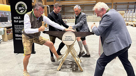 Sageln zur symbolischen Eröffnung der neuen Produktionshalle: Penzkofer-Geschäftsführer Alexander Penzkofer (l.) und Minister Alois Rainer (r.) griffen am Baumstamm gemeinsam zur Zugsäge, unterstützt von stellvertretendem Geschäftsführer Alexander Hartl und Ronny Raith.