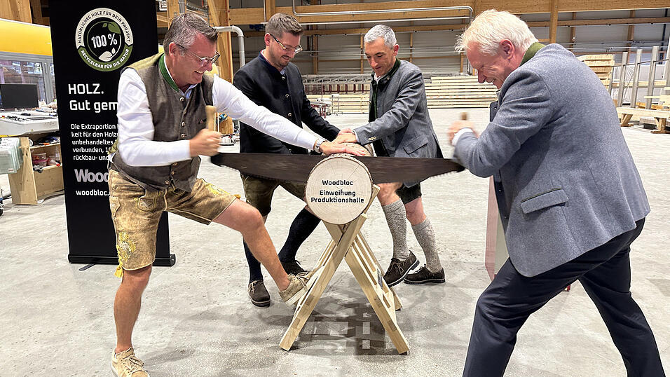 Sageln zur symbolischen Eröffnung der neuen Produktionshalle: Penzkofer-Geschäftsführer Alexander Penzkofer (l.) und Minister Alois Rainer (r.) griffen am Baumstamm gemeinsam zur Zugsäge, unterstützt von stellvertretendem Geschäftsführer Alexander Hartl und Ronny Raith.