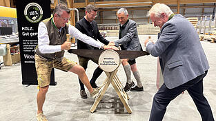 Sageln zur symbolischen Eröffnung der neuen Produktionshalle: Penzkofer-Geschäftsführer Alexander Penzkofer (l.) und Minister Alois Rainer (r.) griffen am Baumstamm gemeinsam zur Zugsäge, unterstützt von stellvertretendem Geschäftsführer Alexander Hartl und Ronny Raith.