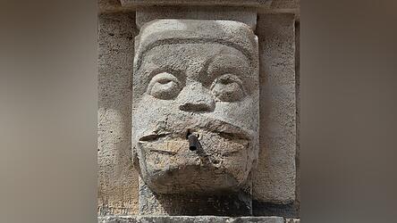 Absicht oder passend? Das Gesicht des Wasserspeiers verdreht die Augen, weil ihm die Lippen abgesprengt wurden.