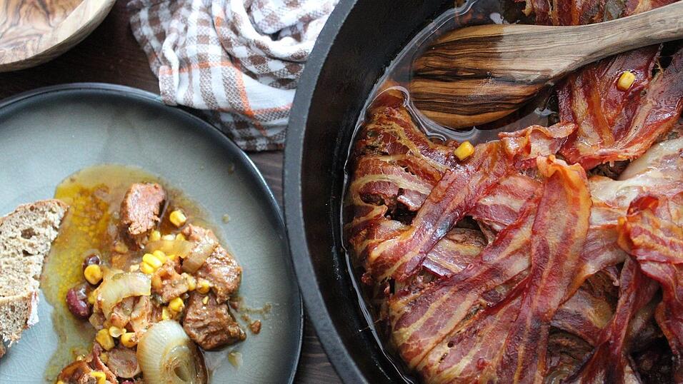 Das amerikanische Gulasch wird im Dutch Oven oder im Bräter zubereitet. Die Innenseite wird mit Frühstücksspeck ausgekleidet.