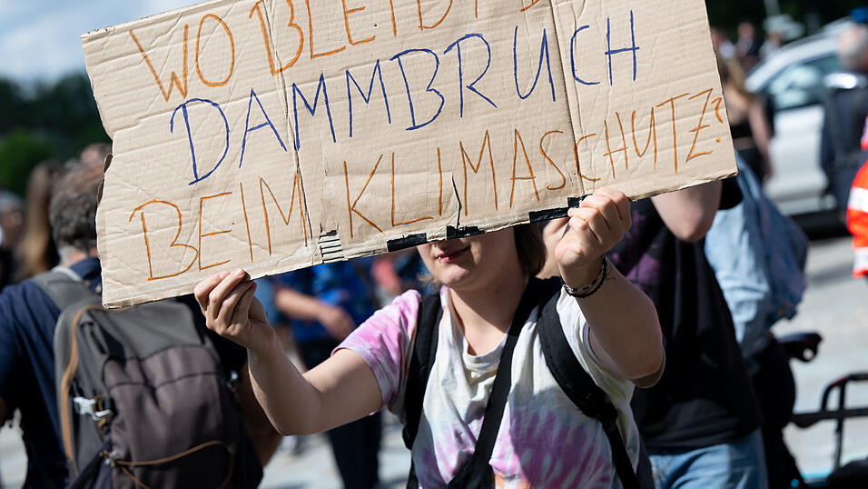 Eine Person hält ein Plakat mit der Aufschrift “Wo bleibt der Dammbruch beim Klimaschutz“ in die Höhe. Eine Person hält ein Plakat mit der Aufschrift “Wo bleibt der Dammbruch beim Klimaschutz“ in die Höhe.