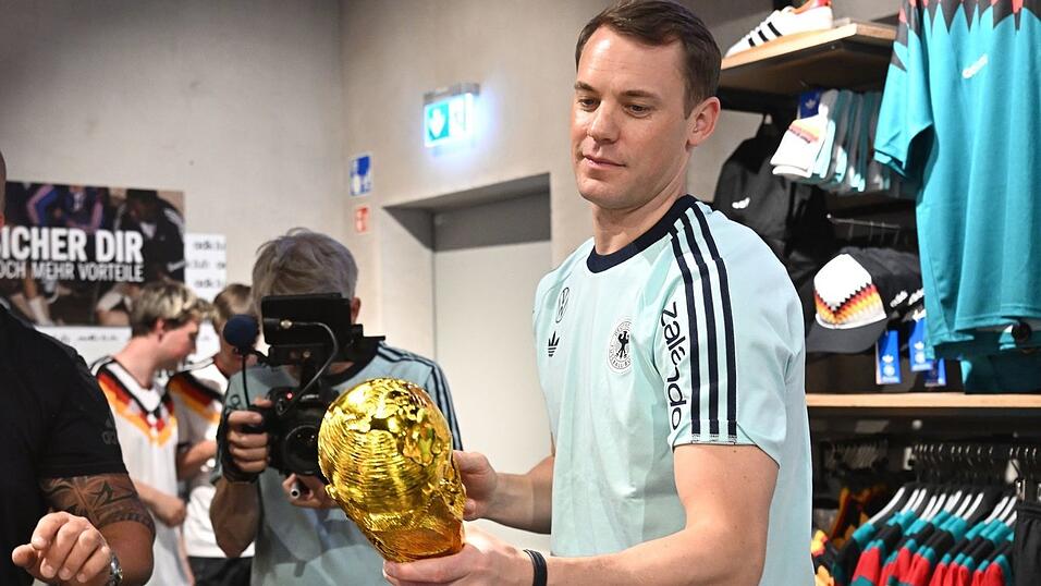 Lächelnd signiert Manuel Neuer einen goldenen WM-Pokal. Lächelnd signiert Manuel Neuer einen goldenen WM-Pokal.