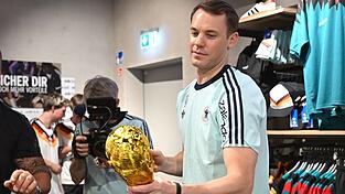 Lächelnd signiert Manuel Neuer einen goldenen WM-Pokal. Lächelnd signiert Manuel Neuer einen goldenen WM-Pokal.