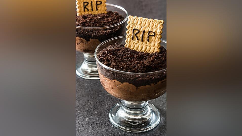 Eine schöne dunkle Mousse au Chocolat findet in den Gläsern ihre letzte Ruhe. Dunkle Keksstreusel bedecken die Mousse und ein heller Keks dient als Grabstein.
