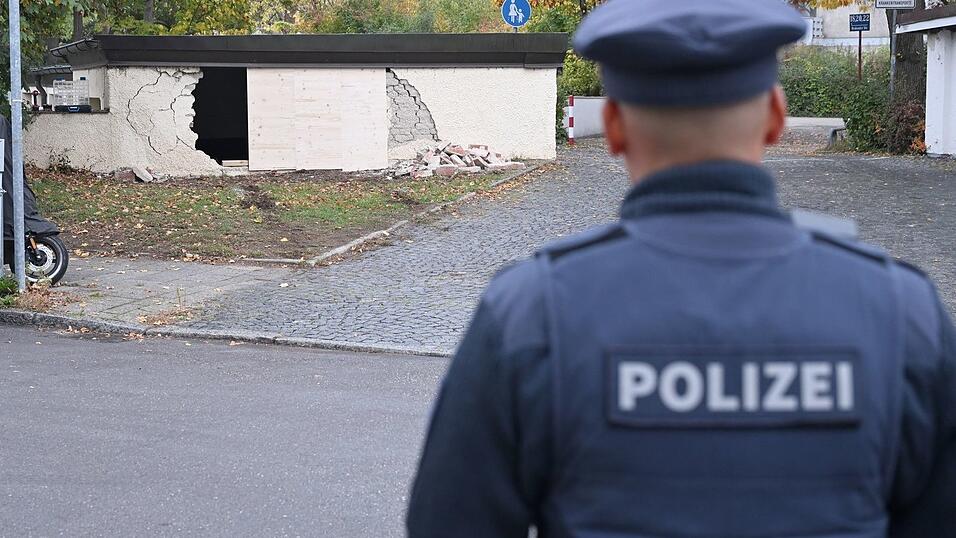Ein Polizist betrachtet die besch&auml;digte Garagenwand.