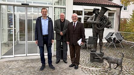 B&uuml;rgermeister Georg Edbauer, Gesch&auml;ftsf&uuml;hrer Michael Trotz und Pfarrer Hans-J&uuml;rgen Koller (v. l.) vor der Fachklinik Schwarzach. Die Statue rechts wurde der Klinik von einem K&uuml;nstler, einem ehemaligen Patienten, gespendet - wen sie darstellt, wei&szlig; niemand.