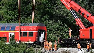 Ein Waggon von dem verunfallten Regionalzug hängt für die Bergung an dem Schienenkran.