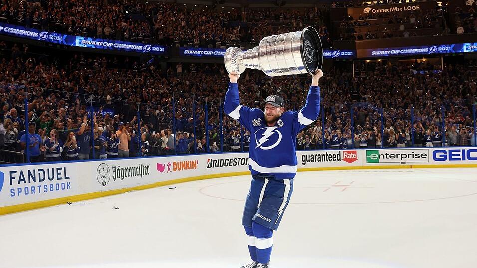 Tampa Bay Lightning verteidigt den Titel in der NHL. Der Kapitän der Mannschaft, Steven Stamkos, fährt mit einem breiten Grinsen und dem Stanley Cup über dem Kopf über das Eis und lässt sich von den Fans feiern. Tampa Bay Lightning verteidigt den Titel in der NHL. Der Kapitän der Mannschaft, Steven Stamkos, fährt mit einem breiten Grinsen und dem Stanley Cup über dem Kopf über das Eis und lässt sich von den Fans feiern.