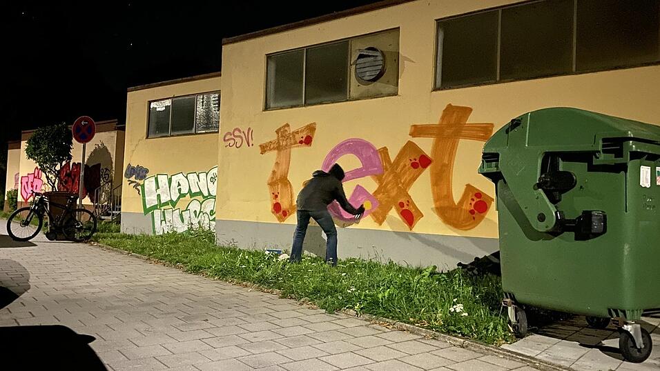 Max trägt dunkle Kleidung, über dem Gesicht eine FFP2-Maske. Er will unerkannt bleiben. Doch im Licht der Straßenlaternen kommt selbst der kleinste Farbklecks auf der buttergelben Wand zum Vorschein.