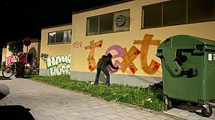 Max trägt dunkle Kleidung, über dem Gesicht eine FFP2-Maske. Er will unerkannt bleiben. Doch im Licht der Straßenlaternen kommt selbst der kleinste Farbklecks auf der buttergelben Wand zum Vorschein.