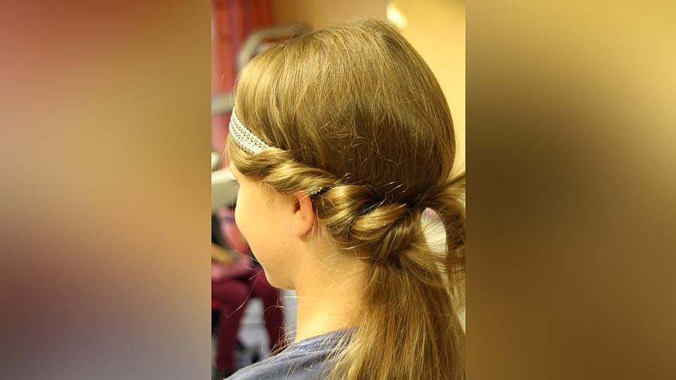 2. Dann nimmt sie von einer Seite eine Haarstr&auml;hne, legt sie locker um das Haarband und schiebt sie von oben nach unten in das Band. Dabei arbeitet sie von vorne bis zur Mitte des Hinterkopfes und beginnt dann von der anderen Seite. Haare, die noch wegstehen, fixiert sie mit Haarnadeln. Das Ganze sollte ruhig etwas locker und unordentlich aussehen, nicht so streng wie bei einem Dutt.