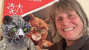 Puppenspielerin Linde Scheringer mit einem ihrer Hauptcharaktere, einer Katze, vor dem diesj&auml;hrigen Figurentheaterfestival-Plakat mit Katze Matou.