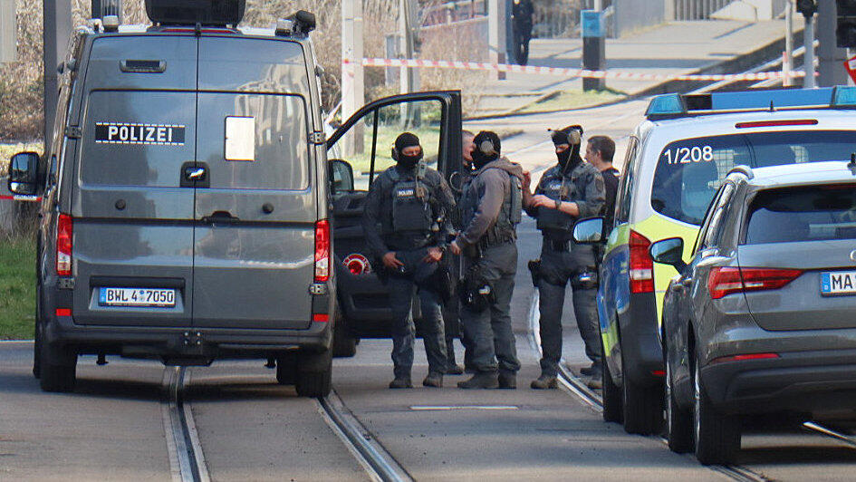 Beamte des Entschärfungsdienstes der Polizei stehen in der Nähe eines beschädigten Fahrzeugs vor einer Zufahrt zur Rheinbrücke. Nach einem Vorfall mit einem Auto in der Mannheimer Innenstadt mit mindestens einem Toten und mehreren Verletzten ist der mutmaßliche Fahrer nach Polizeiangaben festgenommen worden. Nach Polizeiangaben war ein Fahrzeug in eine Menschenmenge gefahren.