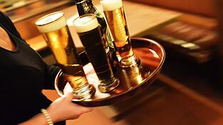 Ein Kellner bringt ein Tablett mit Bier an den Tisch.