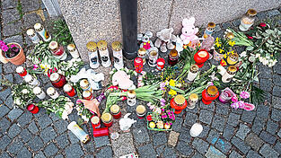 An der Stra&szlig;enecke zur Zufahrtsstra&szlig;e zum Kinder- und Jugendhilfezentrum, in dem eine Zehnj&auml;hrige tot aufgefunden wurde, liegen Blumen, Kuscheltiere und Grablichter auf dem Gehweg.
