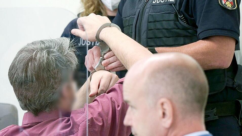 Ein Justizbeamter nimmt dem Angeklagten (l) vor dem Landgericht die Handschellen ab. Im Vordergrund sitzt dessen Anwalt, Axel K&uuml;ster.