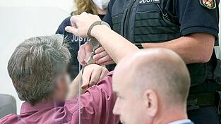 Ein Justizbeamter nimmt dem Angeklagten (l) vor dem Landgericht die Handschellen ab. Im Vordergrund sitzt dessen Anwalt, Axel K&uuml;ster.