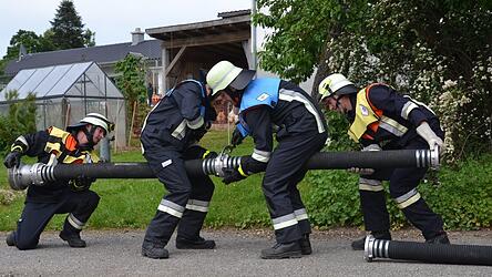 Vier Feuerwehrleute kuppeln eine Saugleitung etwa f&uuml;r die L&ouml;schwasserentnahme aus einem Weiher.
