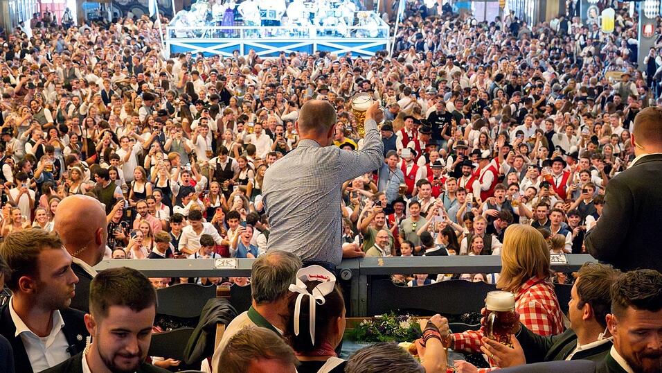 Bundeskanzler Friedrich Merz (CDU) prostet bei seinem Besuch des Oktoberfests Bierzeltbesuchern von der Empore in der Festhalle Schottenhamel zu.