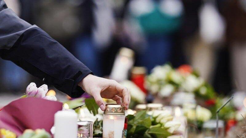 Menschen legen vor einem Geb&auml;ude der Universit&auml;t Blumen und Kerzen an den Wegesrand.