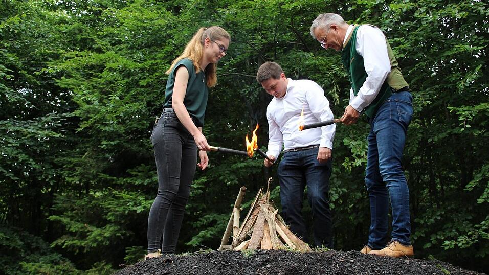 Frauke Holland, Dominik Schwarz und Markus Ackermann (von links) z&uuml;nden den Kohlenmeiler an.