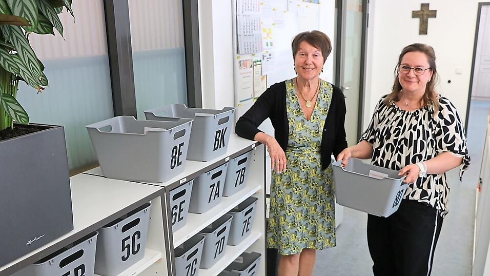 Ursula Weger (links), Schulleiterin des Gymnasiums Seligenthal, und Schulsekret&auml;rin Christine Brandstetter mit den Kisten, mit denen morgens vor dem Unterricht die Smartphones und Smartwatches eingesammelt werden.