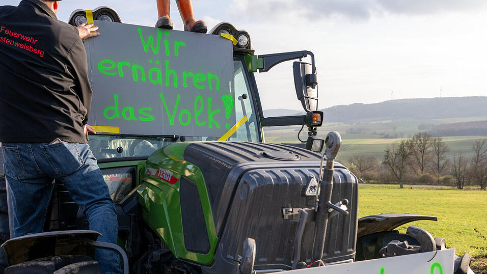Ein Landwirt befestigt ein Protestschild an seinem Traktor.