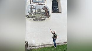 Peter Stoiber zeigt an der Au&szlig;enwand der Kirche zur Heiligen Walburga auf dem Lamberg auf das Bildnis eines J&auml;gers, der einen B&auml;ren erschie&szlig;t.