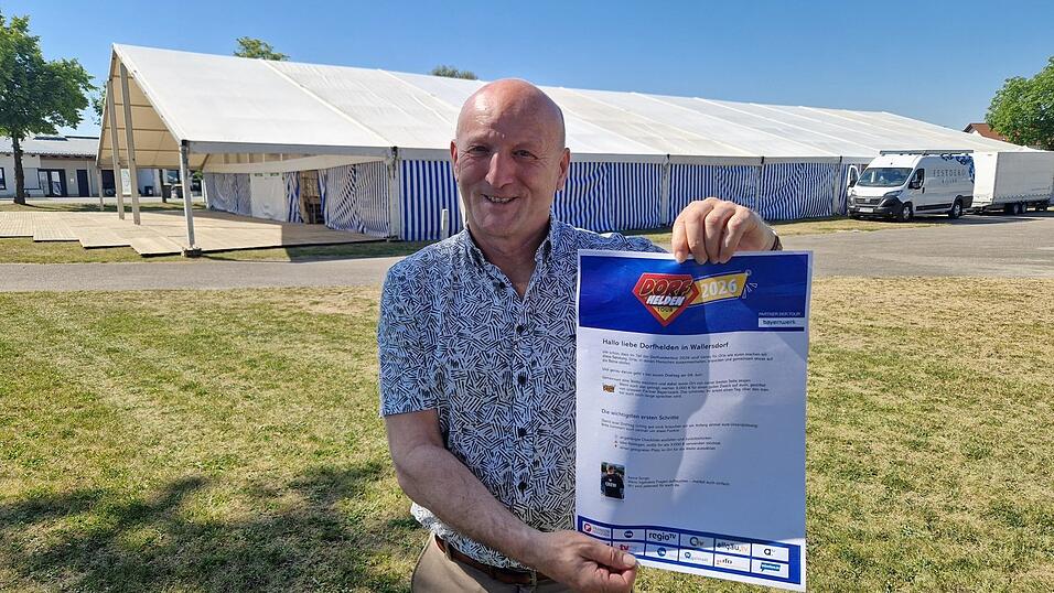 Der Wallersdorfer B&uuml;rgermeister Franz Aster mit dem Plakat zur &bdquo;Dorfhelden-Tour&ldquo;. Diese gastiert am Dienstag, 9. Juni, in der Marktgemeinde. Daf&uuml;r wird das Festzelt - es steht bereits f&uuml;rs Volksfest - genutzt.