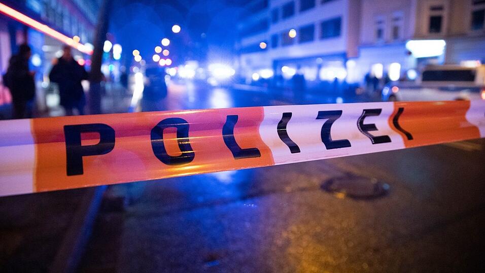 Ein Polizei-Absperrband ist &uuml;ber eine Stra&szlig;e gespannt, auf der eine Menschengruppe marschiert. Die Teilnehmer demonstrieren gegen die aktuellen Corona-Ma&szlig;nahmen.