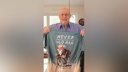 Hans-Josef Ersfeld (85) zeigt sein Motivationstrikot: 'Unterschätze niemals einen alten Mann', steht darauf.