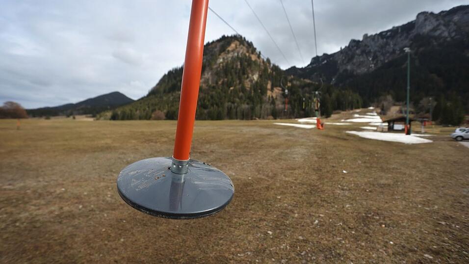 Teller eines Schleppliftes baumeln unbesetzt an einer Skipiste im bayerischen Schwangau, auf der noch Reste von Kunstschnee zu sehen sind.