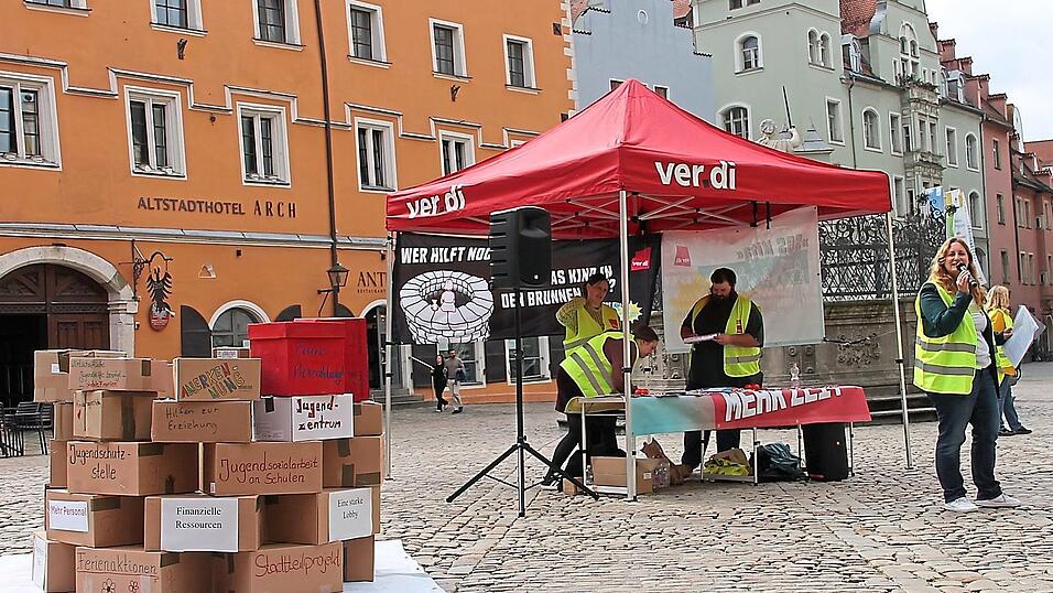 Kathrin Birner (rechts) eröffnet die Kundgebung am Haidplatz. Auf dem Brunnen aus Pappkartons stehen Schlagwörter und Forderungen zur Situation in der Kinder- und Jugendhilfe.