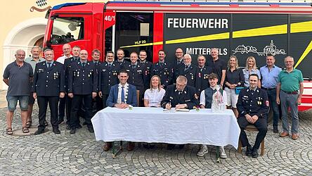Die Marktgemeinde Mitterfels ehrt den neuen KBR Markus Weber (sitzend, Mitte) mit Gattin Daniela und Sohn Patrick mit seinem bereits zweiten Eintrag ins Goldene Buch. Bürgermeister Andreas Liebl (sitzend, links), FFW-Vorsitzender Kilian Graf (sitzend, rechts), und weitere Gäste aus der Feuerwehr und dem Marktgemeinderat begleiteten die Zeremonie und auch das neue HLF 20 (Hilfeleistungslöschgruppenfahrzeug) durfte mit ins Bild.